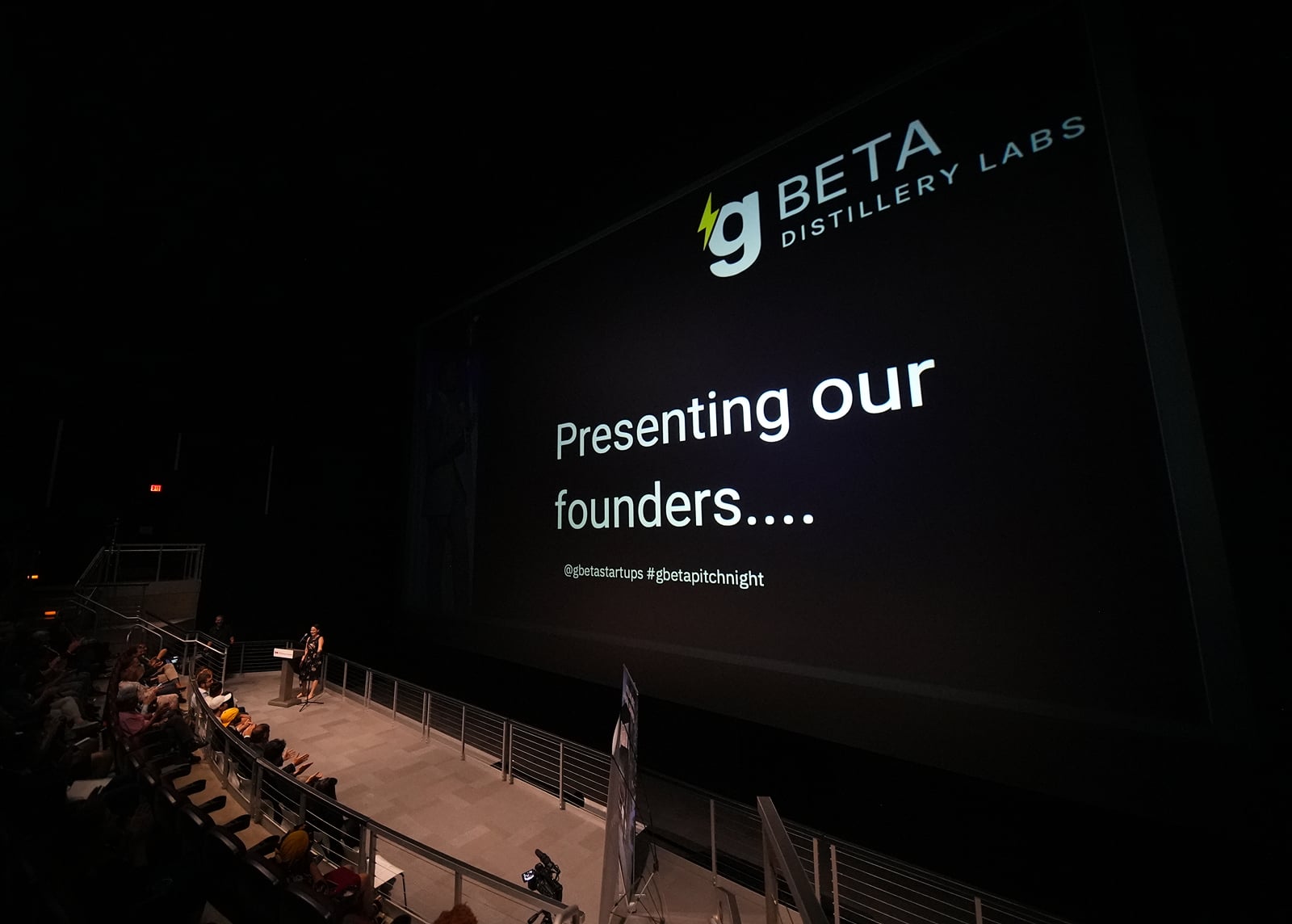 Startup founder presenting at a gBETA accelerator showcase with slides on a large screen