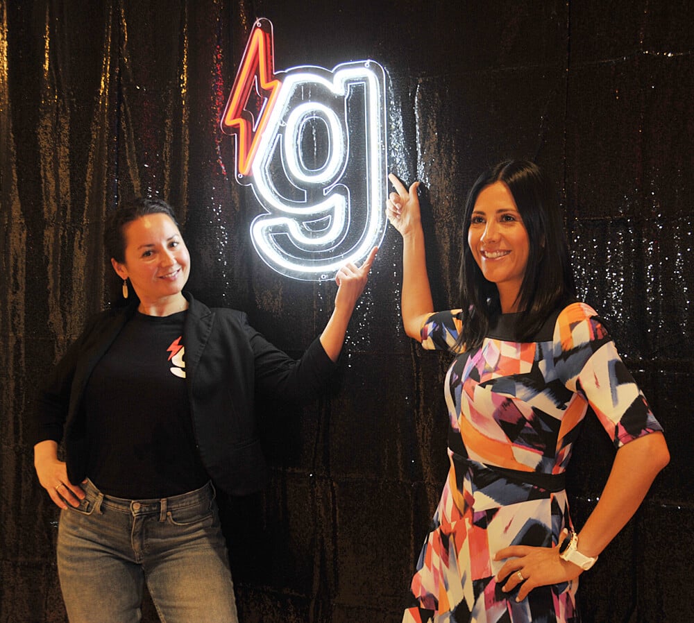 gener8tor team members posing in front of a glowing neon gener8tor sign